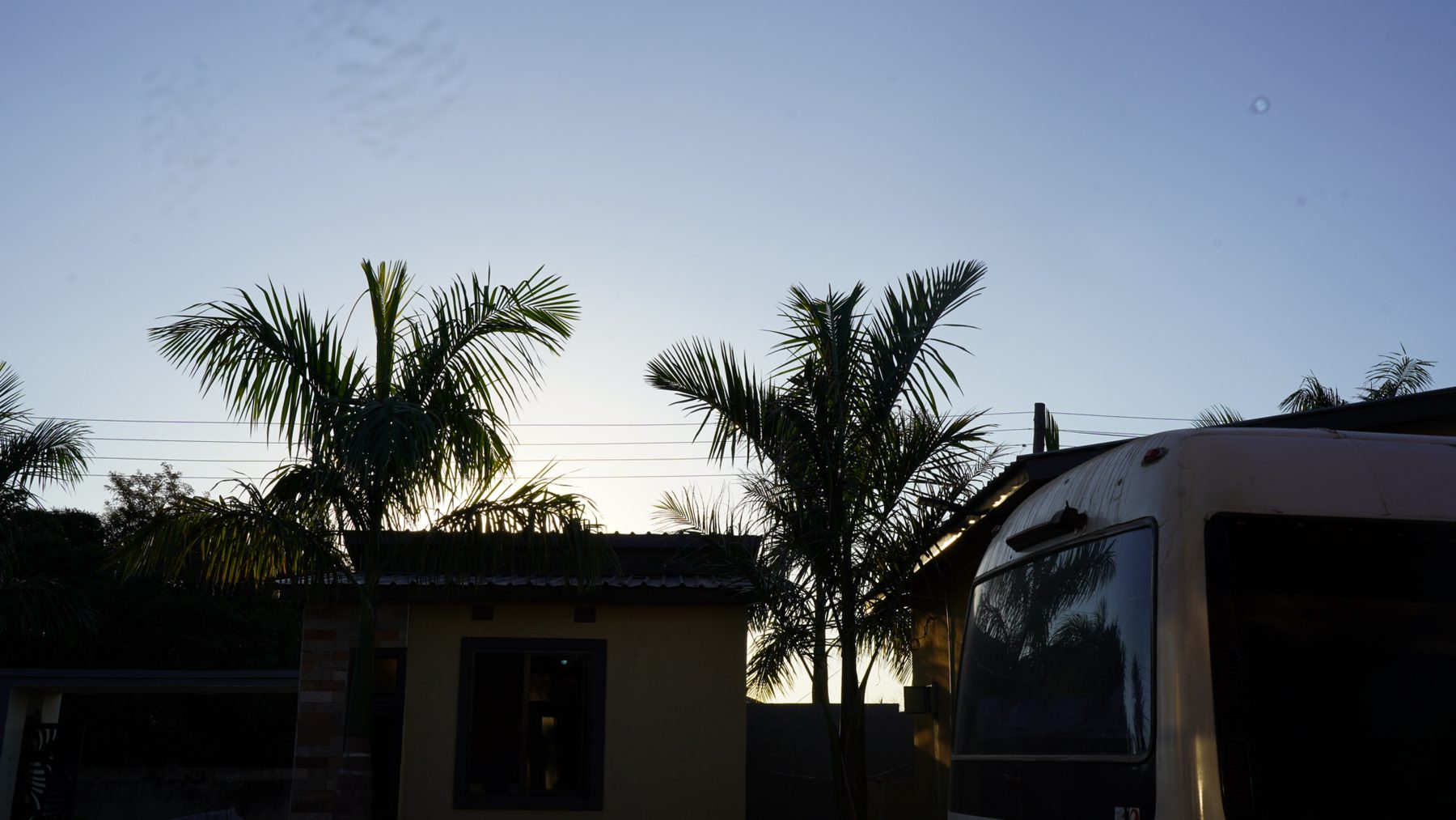 The tour bus parked under palm trees at sunset on arrival in Lusaka, Zambia